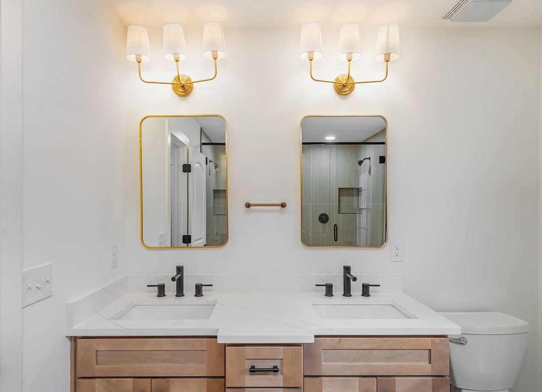 Bathroom with an S2 Honey wood double vanity, brass sconces and gold mirrors
