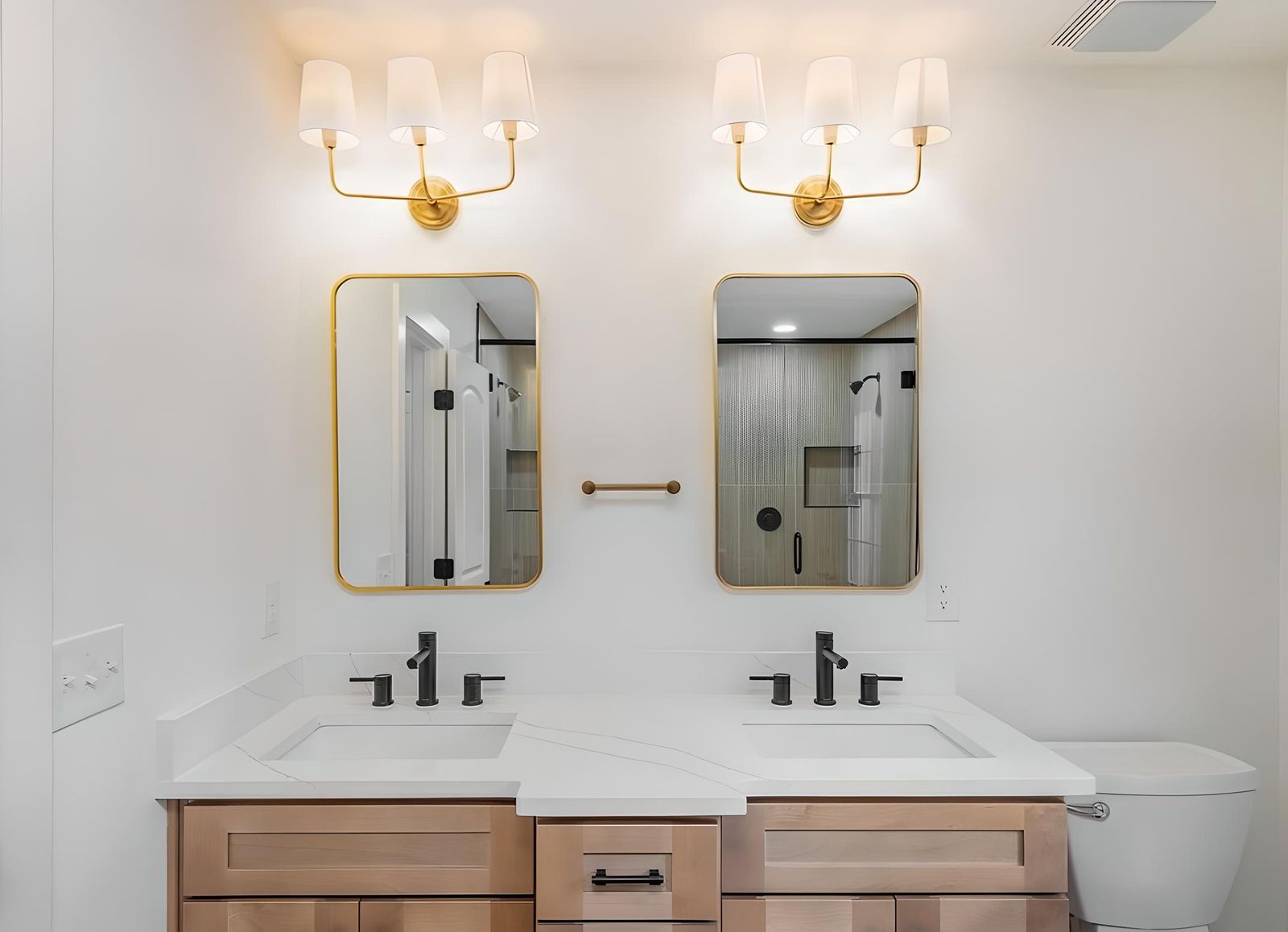 Bathroom with an S2 Honey wood double vanity, brass sconces and gold-framed mirrors