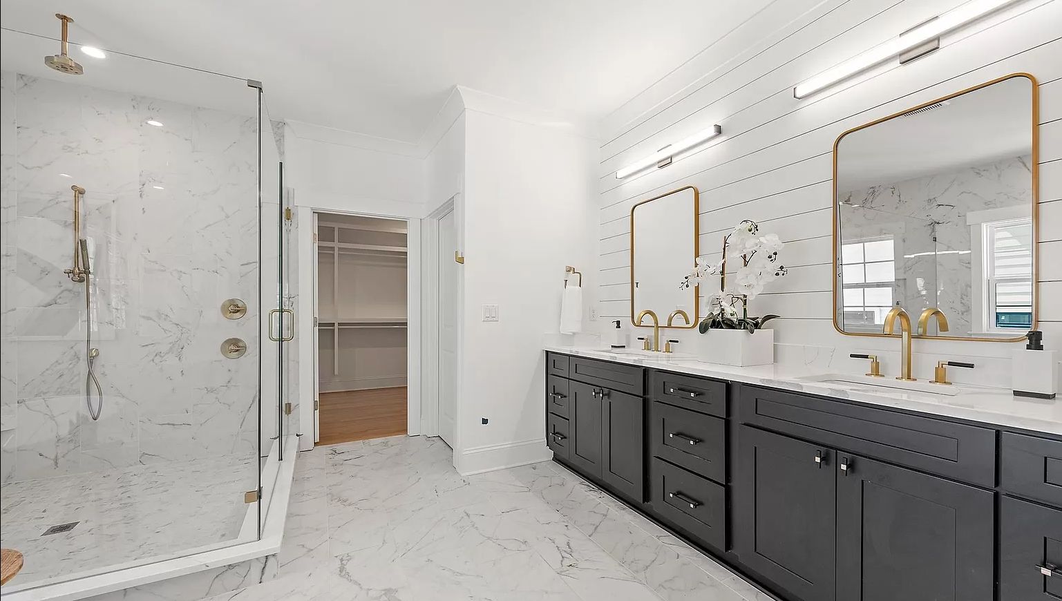 Bathroom with a dark grey double vanity, marble walls and glass shower