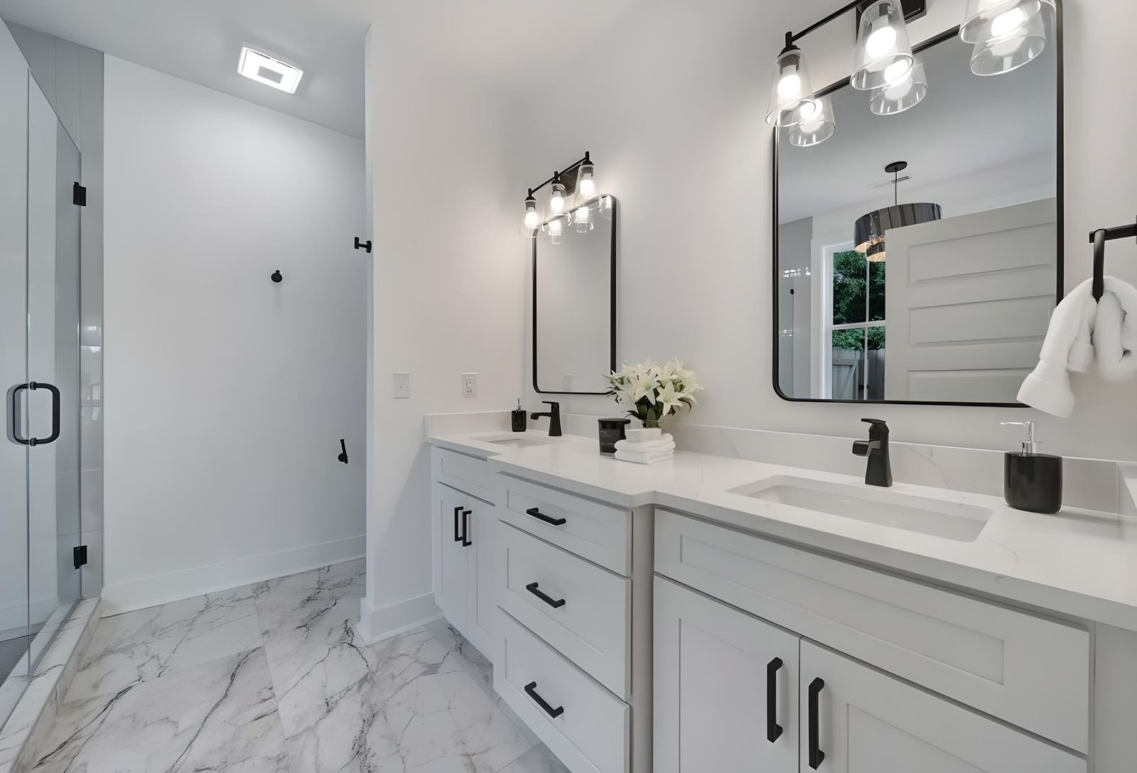 Bathroom with a white shaker double vanity, black fixtures and marble tile
