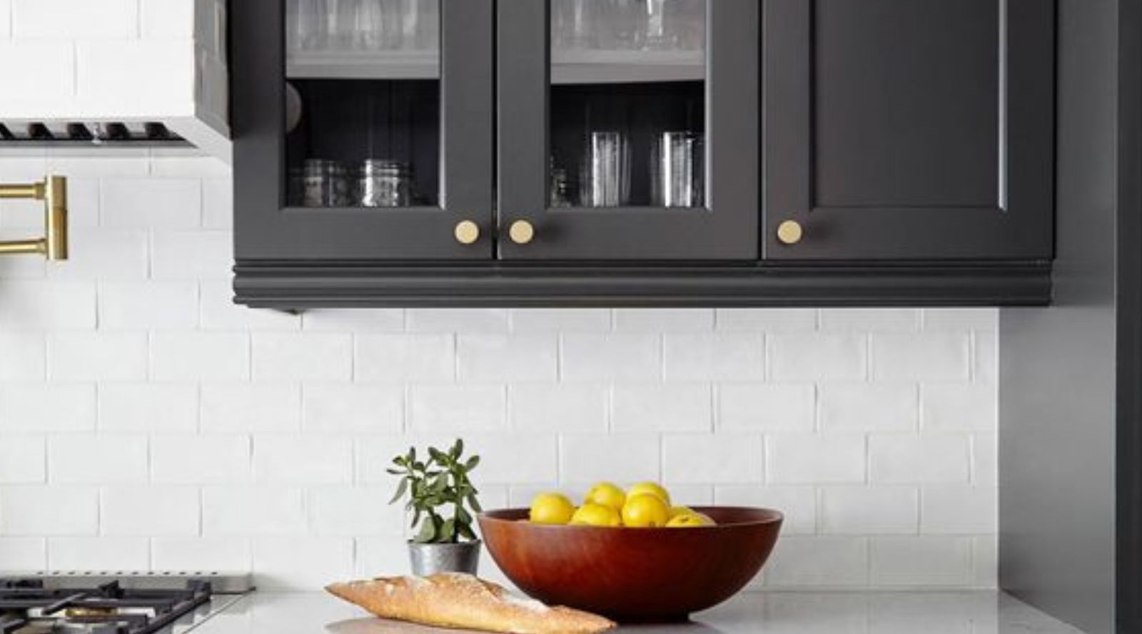 Close-up of D8 Black Swan glass-front upper cabinets over white subway tile with brass pulls