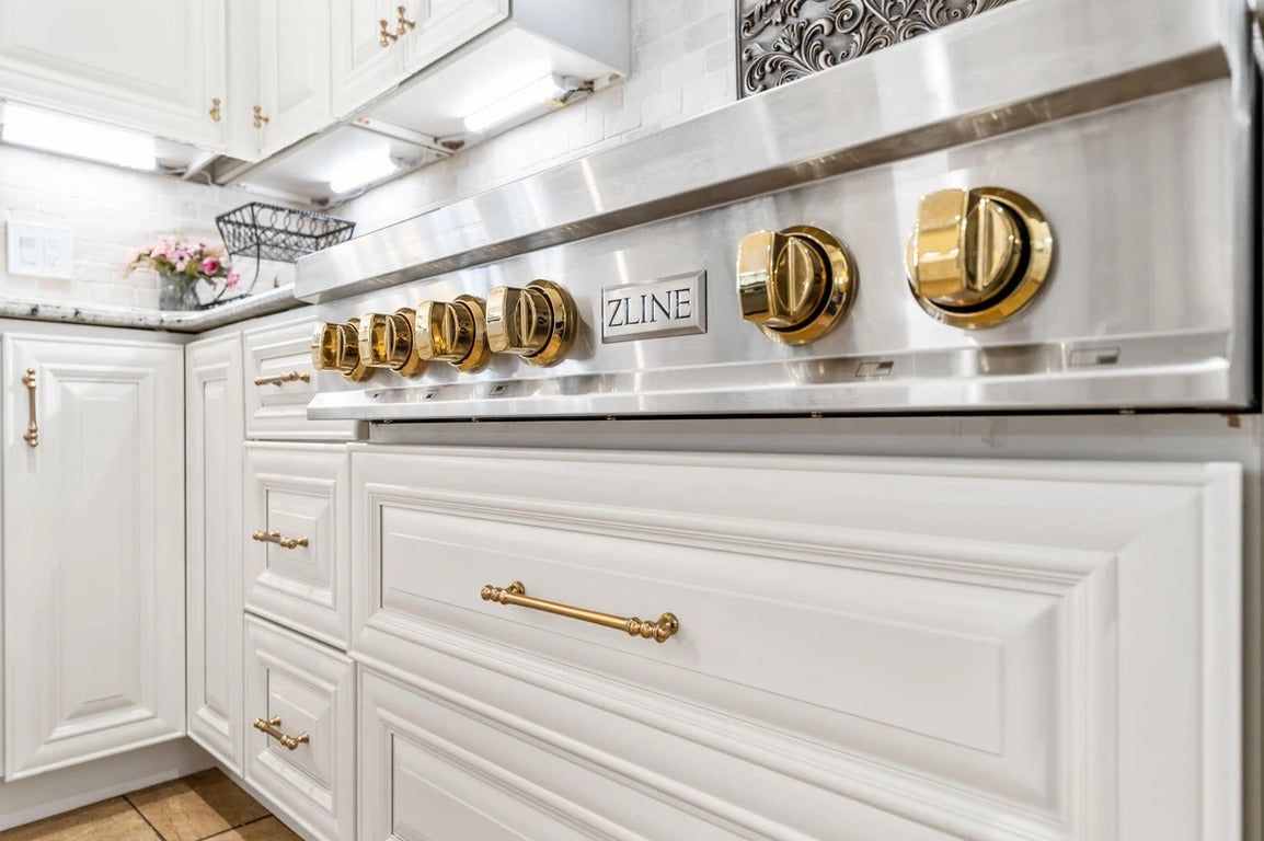 Close-up of D9 Pearl White raised-panel cabinet doors with brass hardware and gold range knobs
