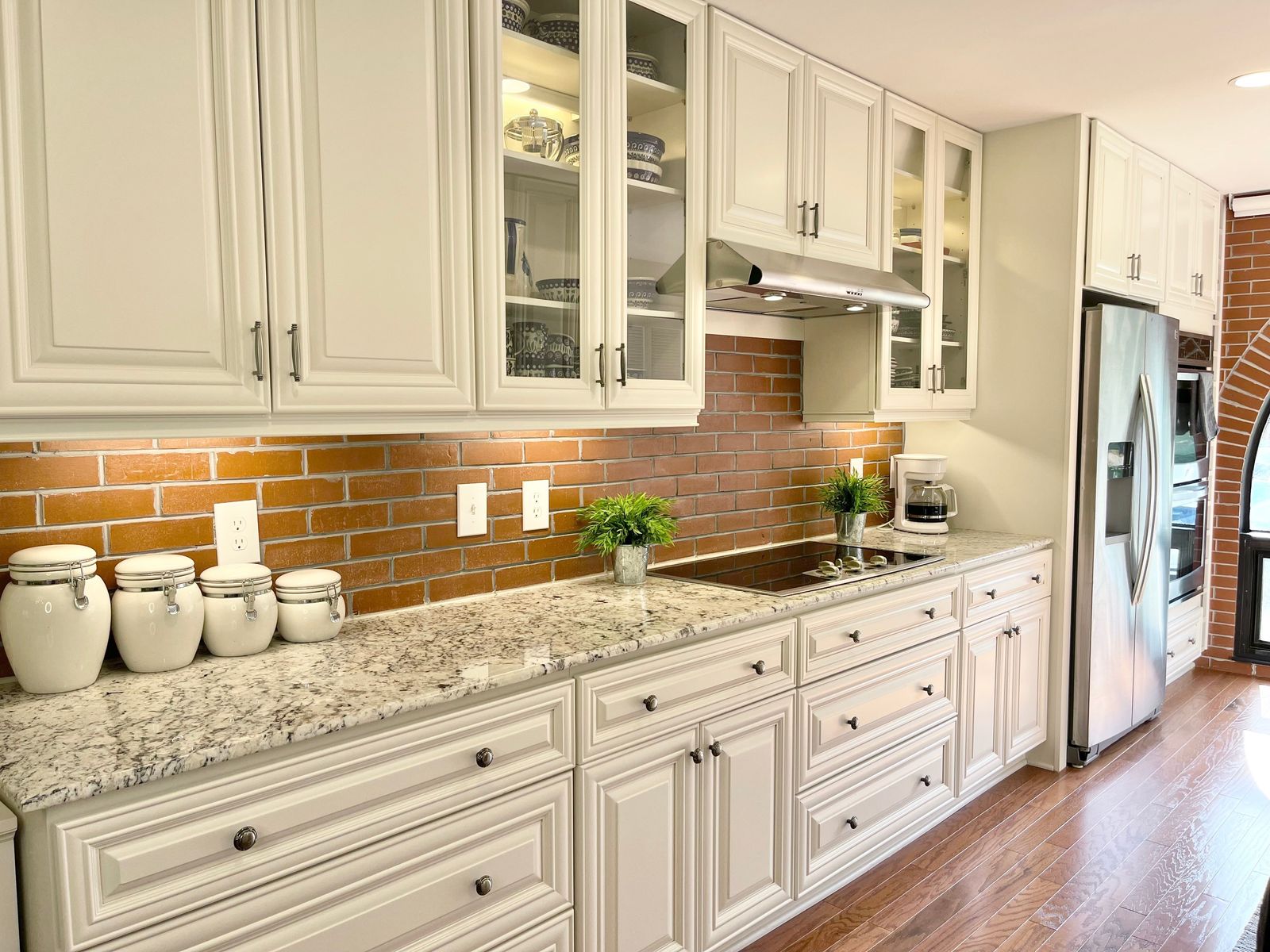 D9 Pearl White raised-panel kitchen cabinets with glass-front uppers and brick backsplash