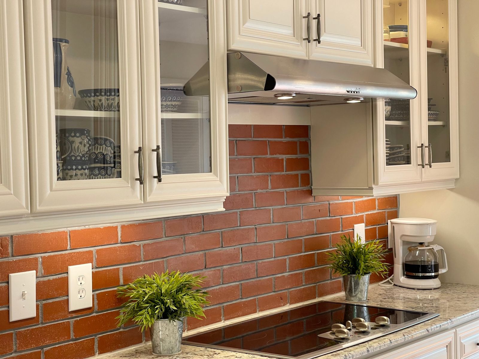 D9 Pearl White raised-panel upper cabinets over a brick backsplash and stainless range hood