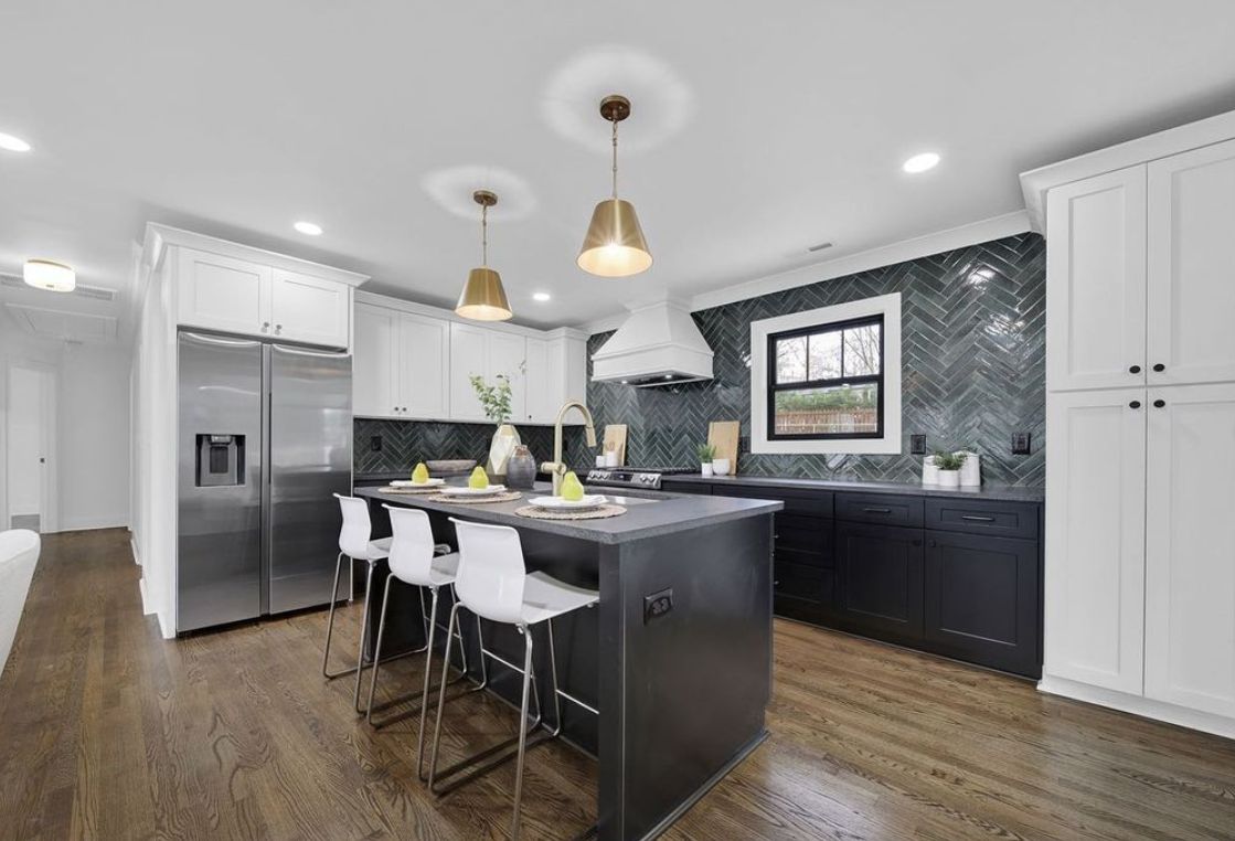 Kitchen with a D8 Black Swan shaker island and white perimeter cabinets, dark herringbone tile backsplash and brass pendants