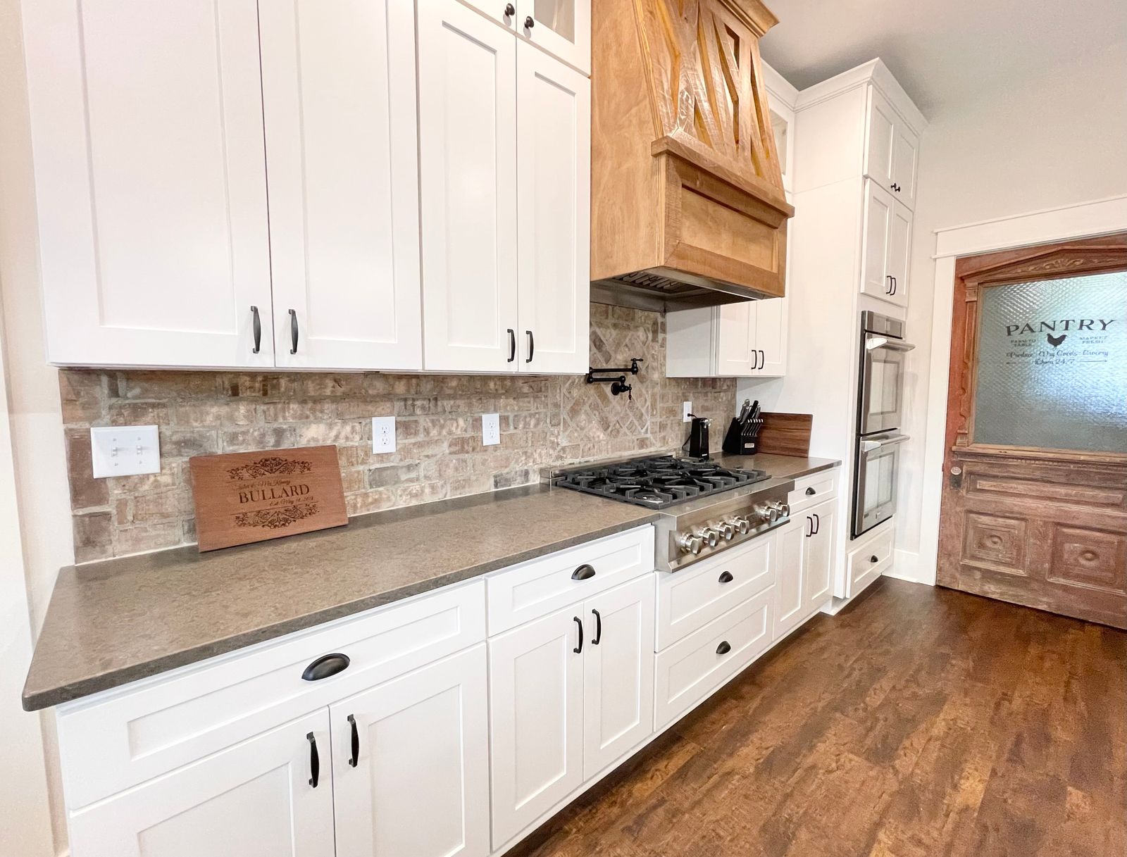 Kitchen with E4 Dusk Wood range hood, white raised-panel cabinets and stone backsplash
