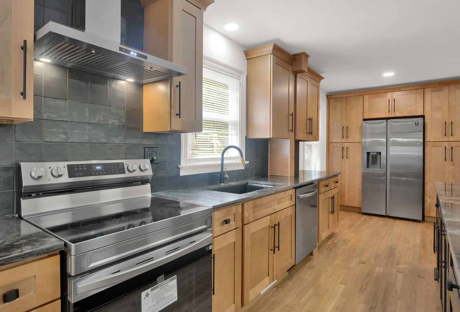 Kitchen with natural wood shaker cabinets, black slate backsplash and stainless range
