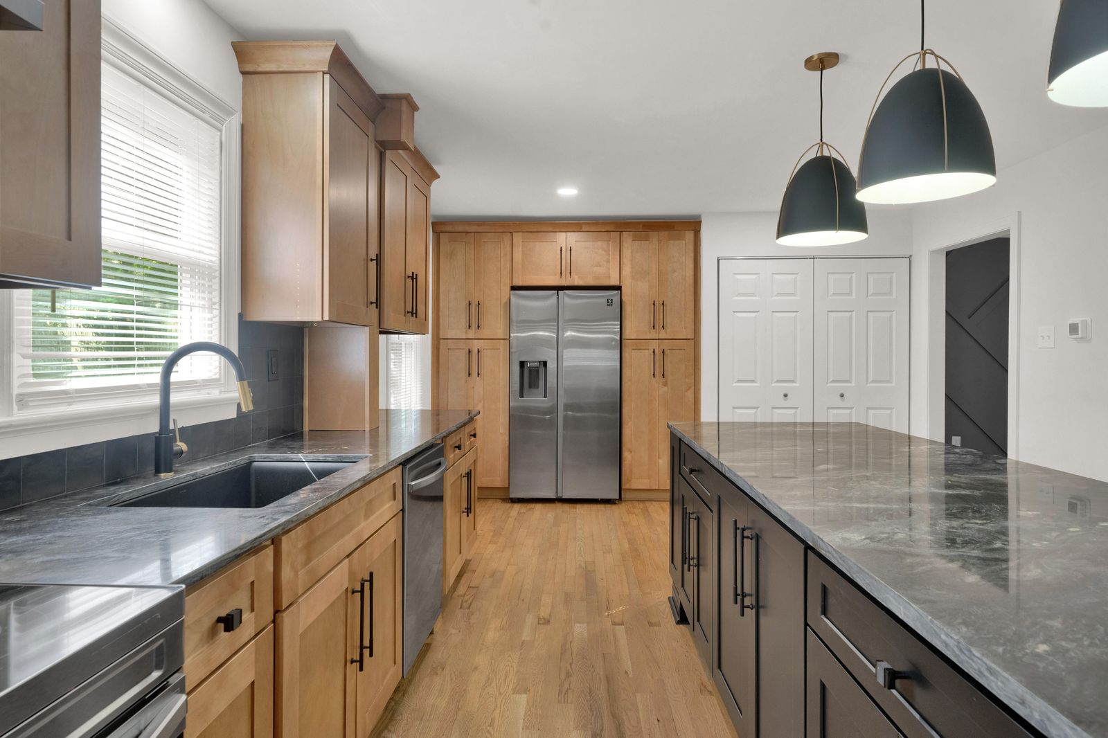 Kitchen with natural wood shaker cabinets, dark grey counters and black pendants