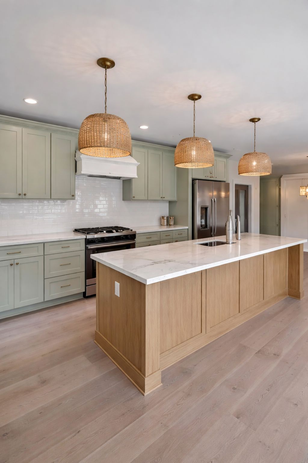 Kitchen with sage green shaker cabinets, white oak island and rattan pendant lights