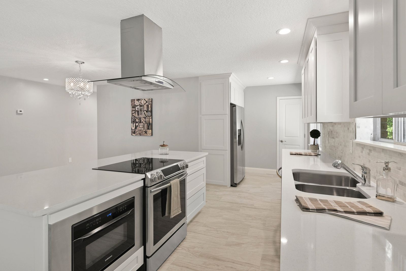 Kitchen with white frameless cabinets, island cooktop and stainless wall oven