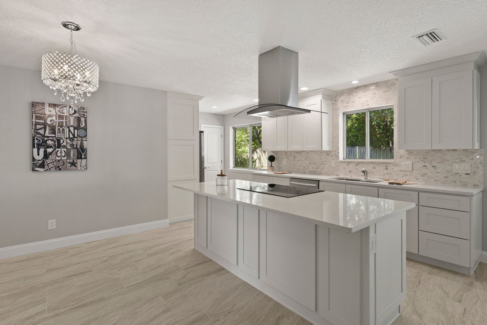 Kitchen with white frameless cabinets, island cooktop and stainless ceiling hood