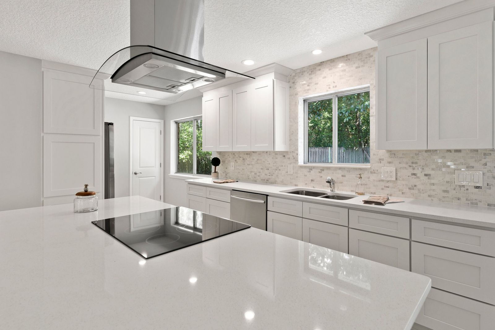 Kitchen with white frameless cabinets, island cooktop and stainless ceiling range hood