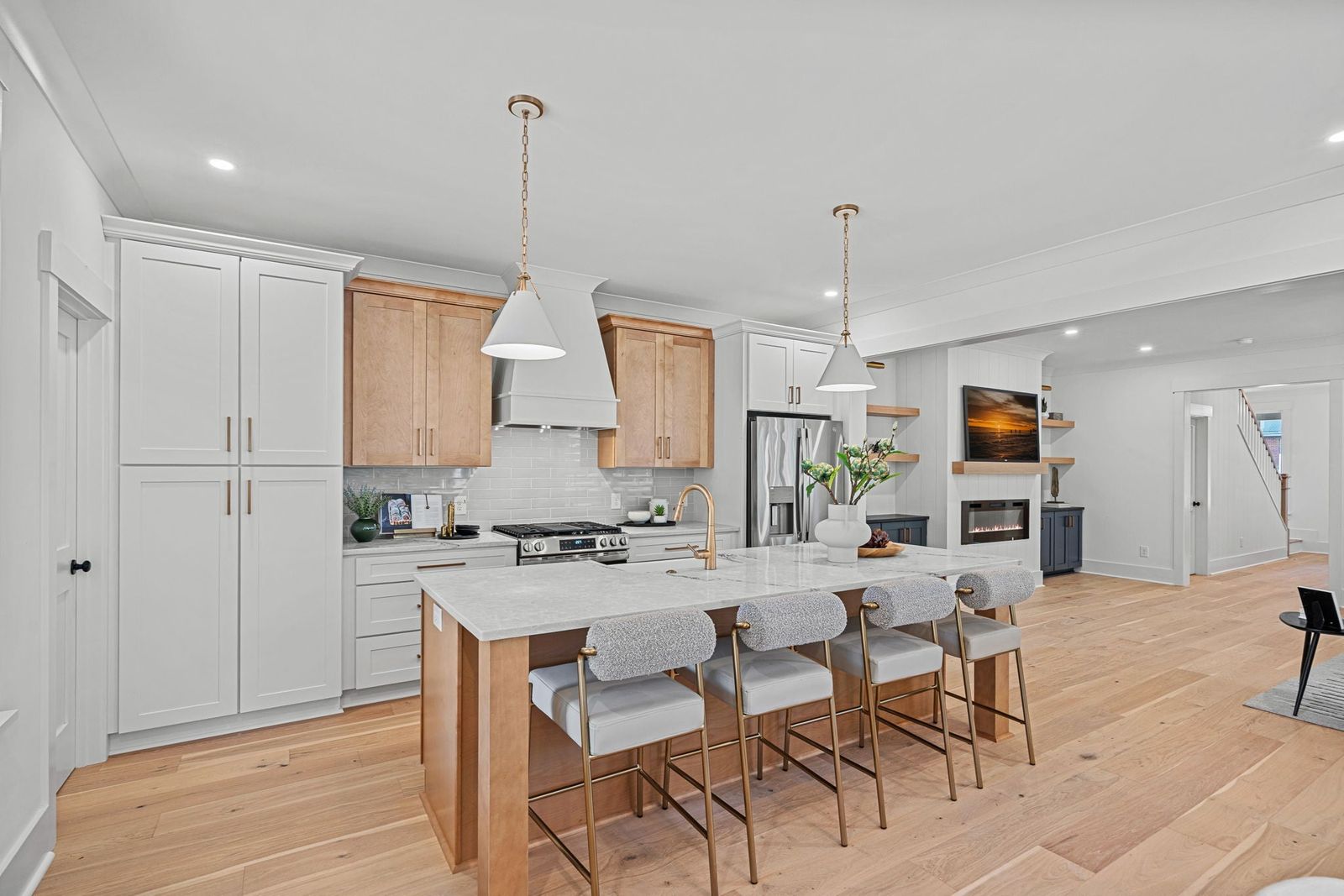 Open-plan kitchen with white shaker cabinets, natural oak island and range hood accents