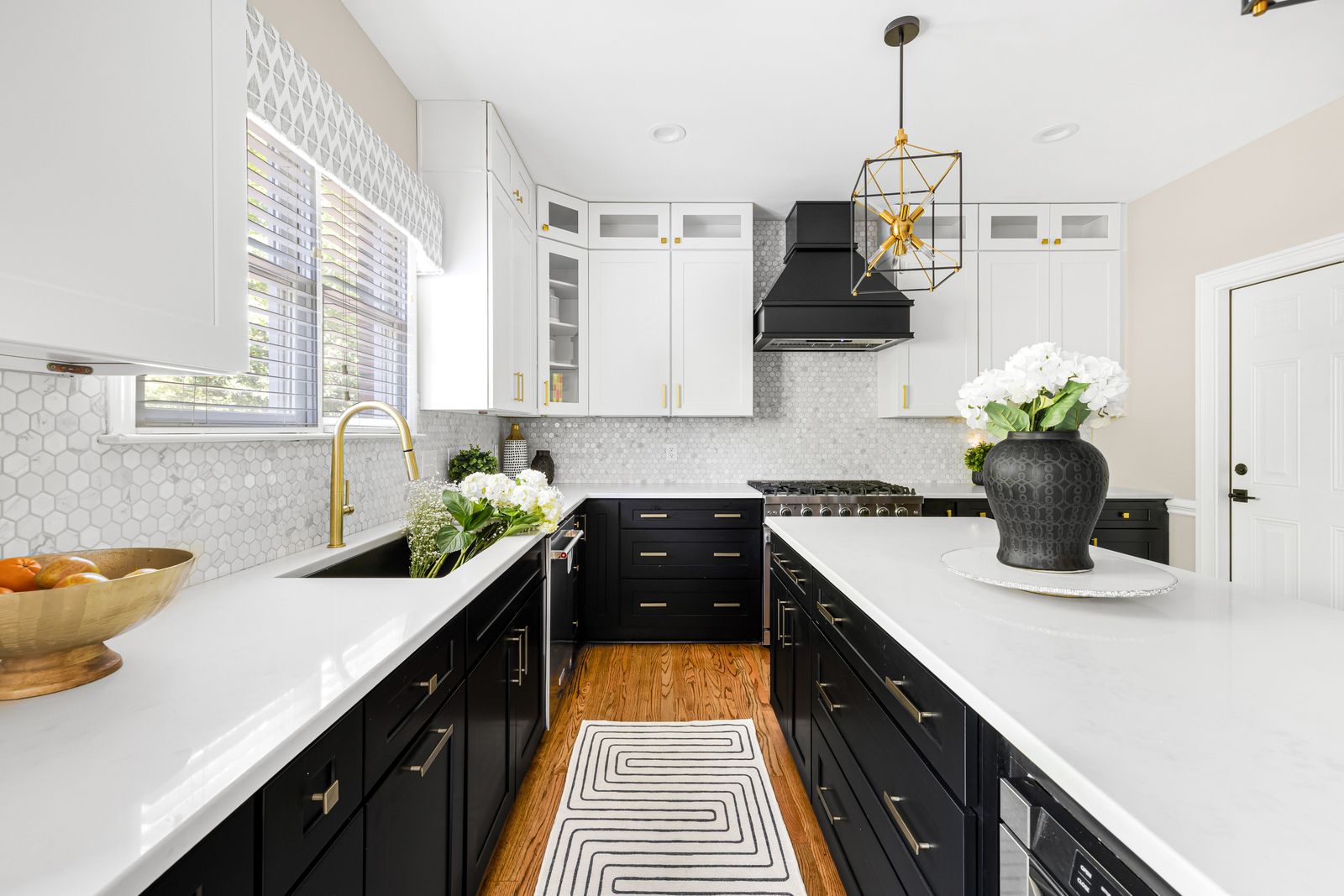 Two-tone kitchen with white uppers and D8 Black Swan base cabinets, black range hood and brass faucet
