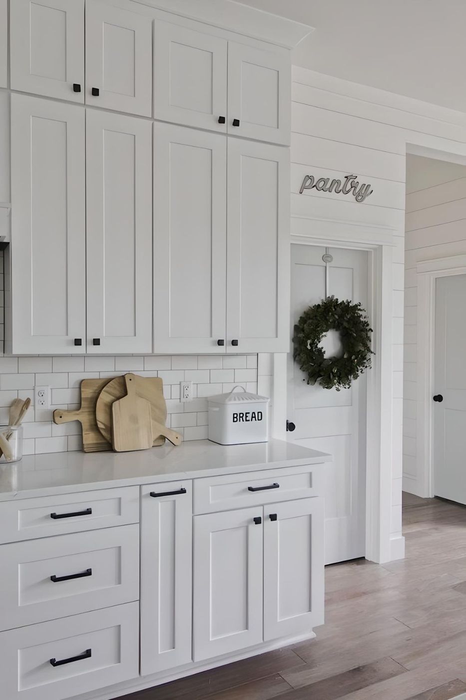 White shaker cabinets beside a farmhouse pantry door with a wreath
