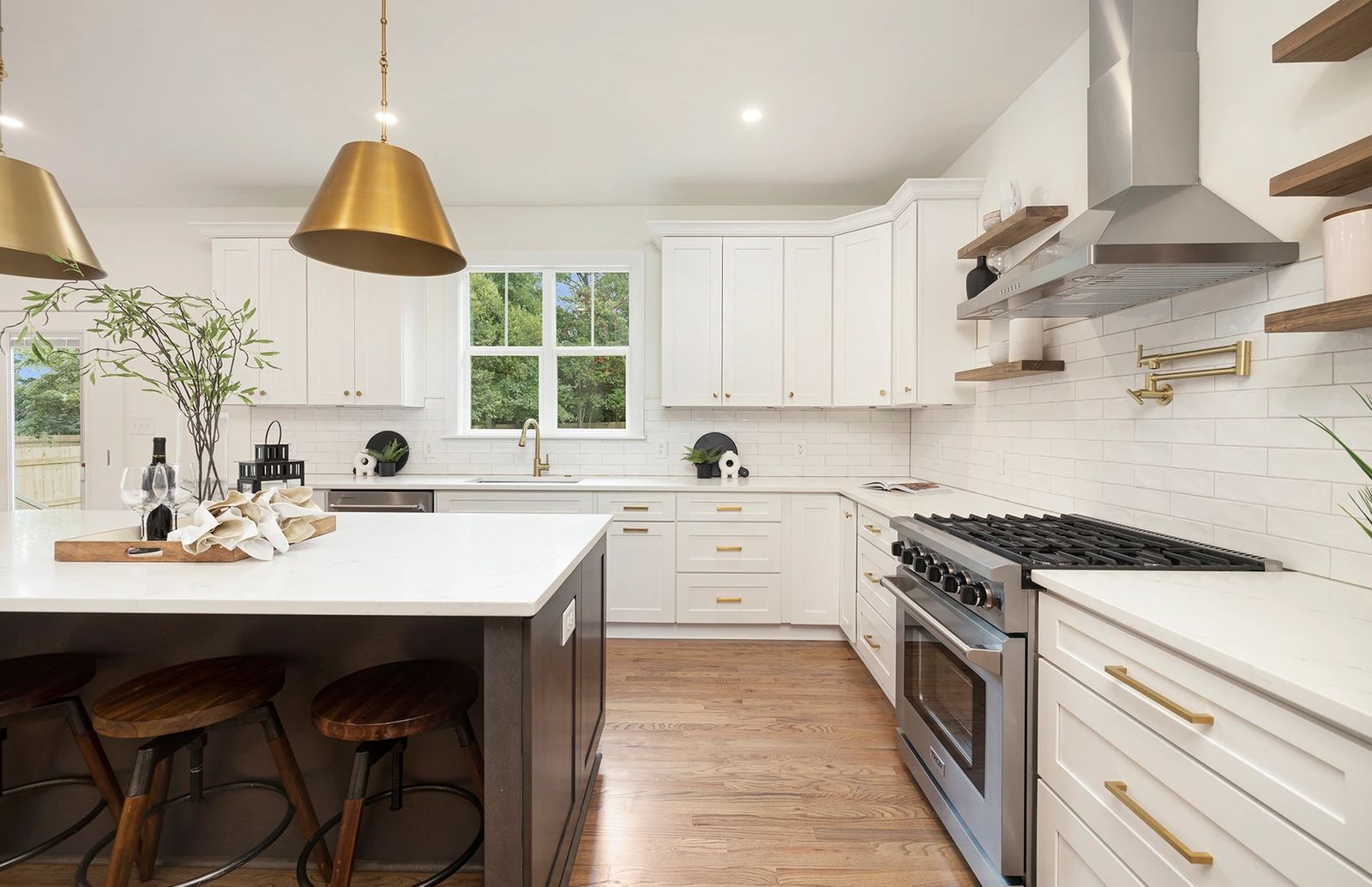White shaker kitchen with a dark island, brass pendants and floating wood shelves