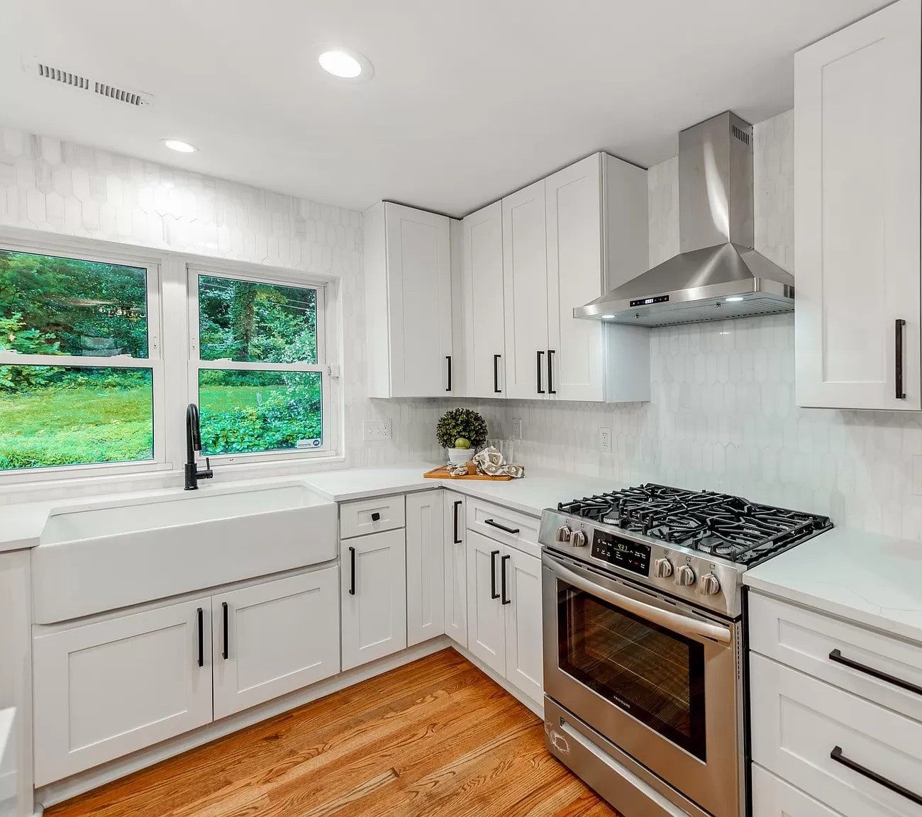 White shaker kitchen with farmhouse sink, black faucet and stainless range hood