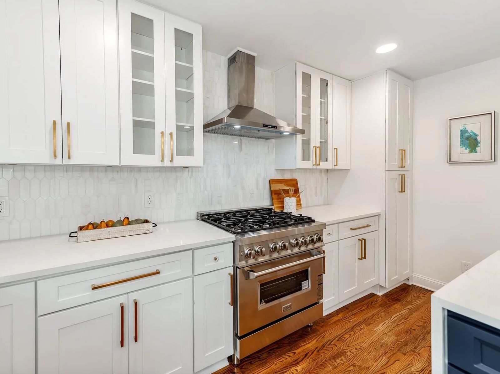 White shaker kitchen with glass-front uppers, stainless range hood and brass pulls