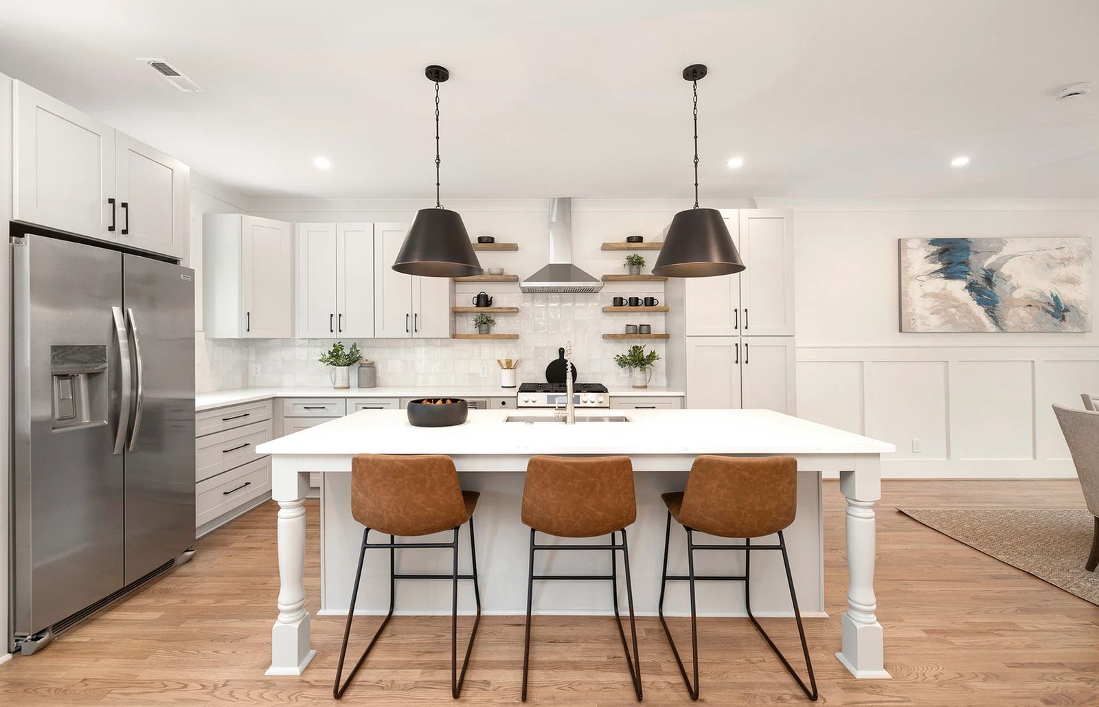 White shaker kitchen with a large island, leather stools and black pendants