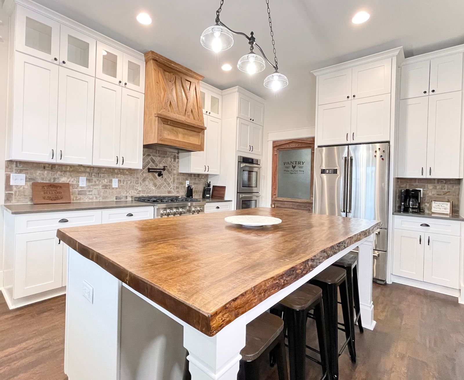 White shaker kitchen with live-edge butcher-block island and glass pendants