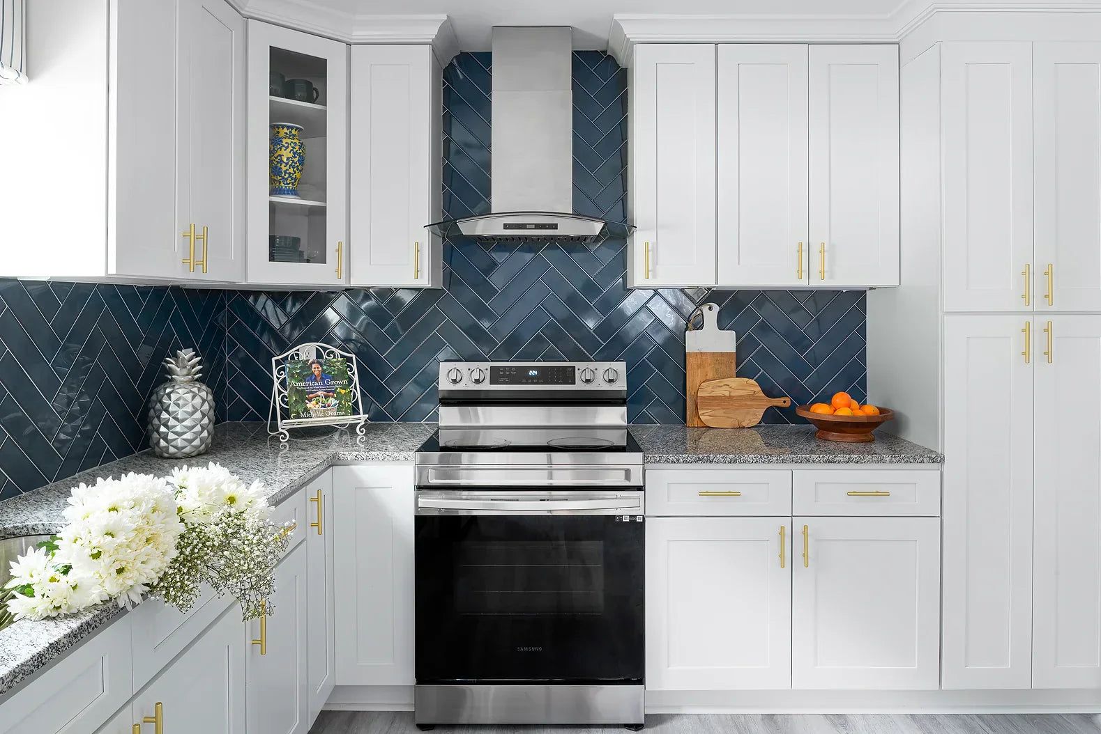 White shaker kitchen with navy herringbone tile backsplash and stainless range hood