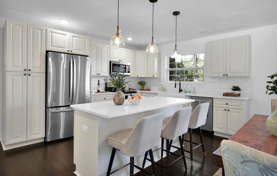 White shaker kitchen with quartz island, glass pendants and stainless refrigerator