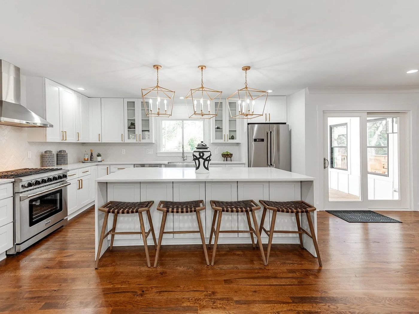 White shaker kitchen with quartz island, wood stools and glass pendants