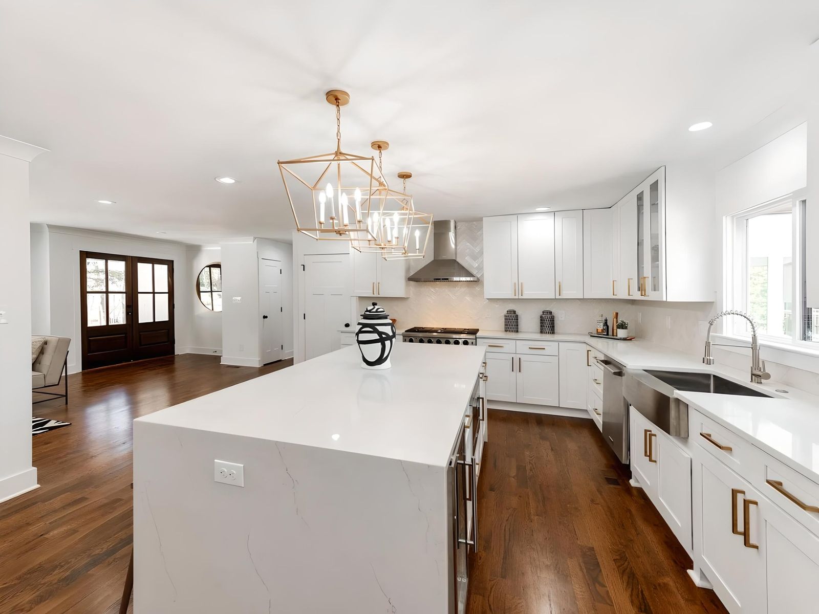 White shaker kitchen with waterfall quartz island, black range hood and brass pendants